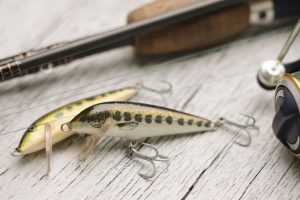 Close-up of fishing lures with rod on wooden background.