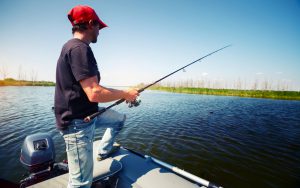Fisherman with rod in the boat on the pond at sunny day